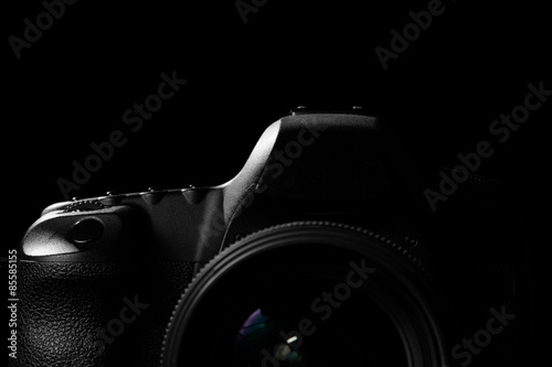 Image of a professional modern DSLR camera low key image - Modern DSLR camera with a very wide aperture lens on in a dark space. Top part of a camera is visible and the rest goes into the shadow photo
