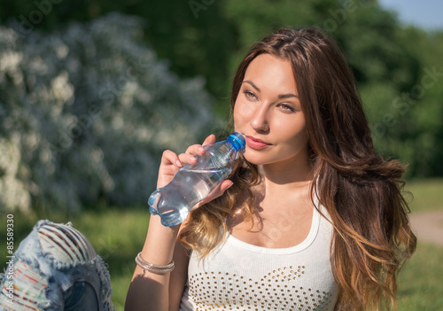 Beautiful girl in a white shirt is drinking water from a bottle
