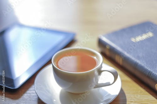 Near a cup the tablet and the Bible lies.