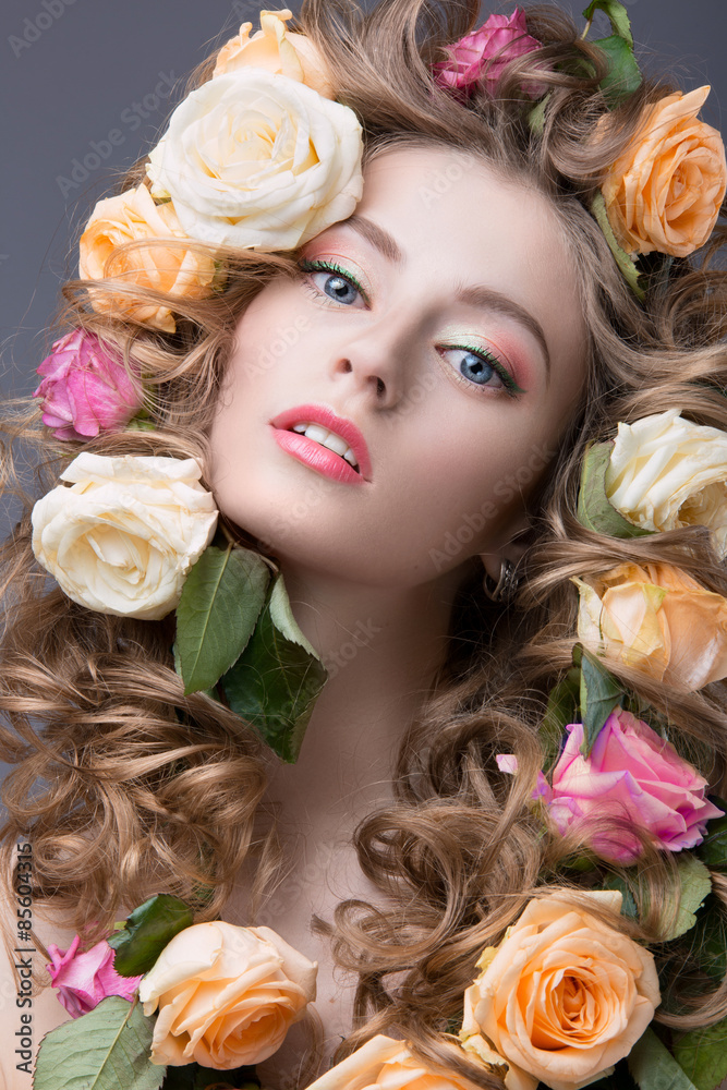 Portrait of a beautiful girl with a gentle pink make-up and lots of flowers in her hair. Spring image. Beauty face. Picture taken in the studio on a gray background.