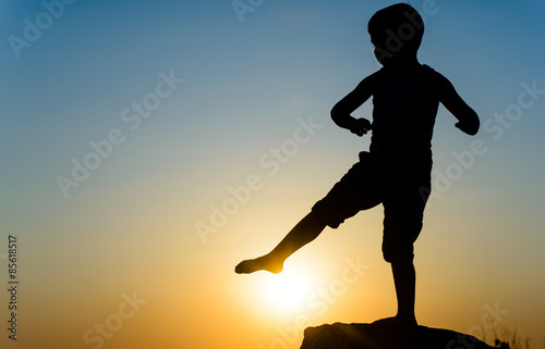 Fototapeta Naklejka Na Ścianę i Meble -  Little boy kicking the setting sun