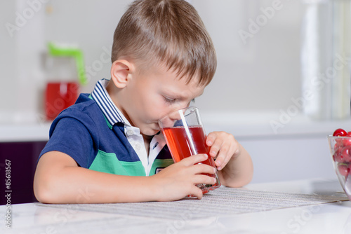 Little boy drinking fruit juice in a kitchen