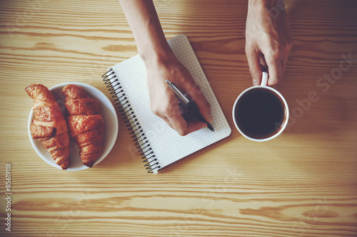 Obraz na płótnie Hands with pen writing on notebook with morning coffee and crois