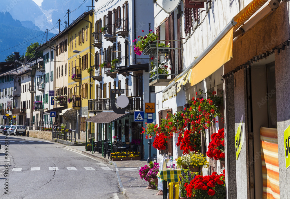 Fototapeta premium Road in alpine village with red flowers on house balcony
