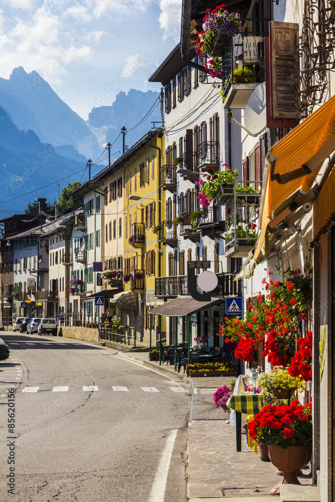 Fototapeta premium Road in alpine village with red flowers on house balcony