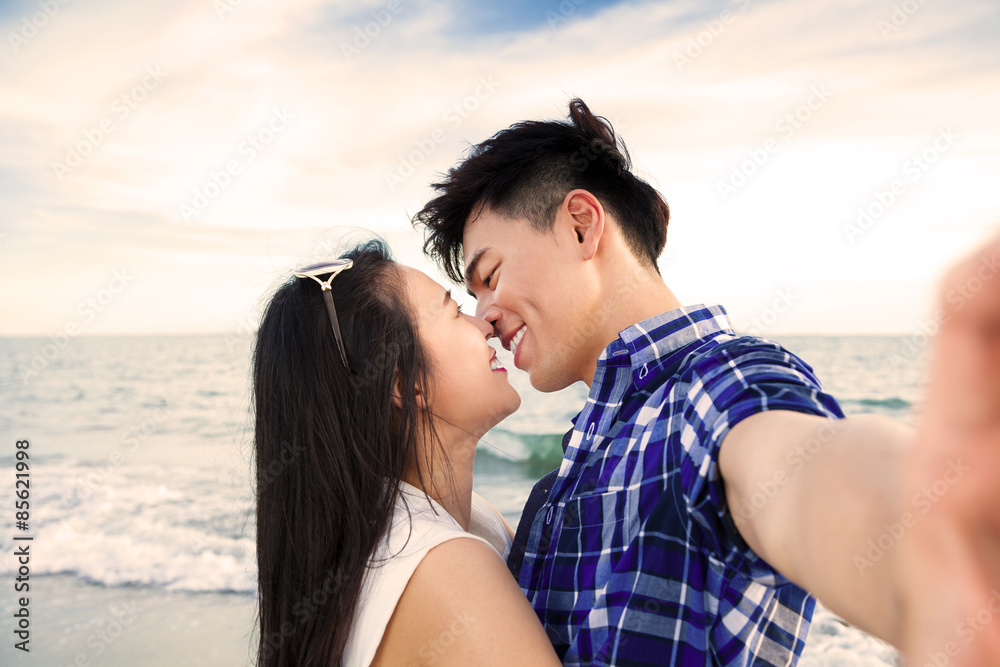 Fototapeta premium Couple taking self portrait photos with smart phone on the beach