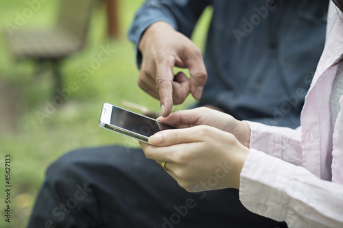 The couple are looking at a smart phone sitting on a bench