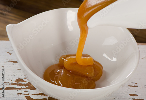 Caramel sauce pouring in  white bowl.