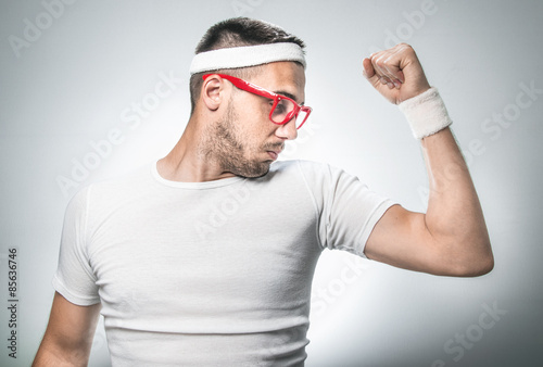 Schilderij op canvas Funny sport man showing his small muscle, weakly nerd, isolated on gray backgoru