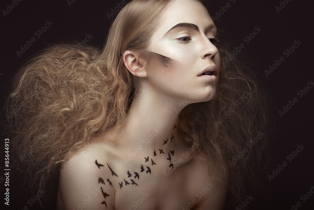 Beautiful girl with a pattern on the body in the form of birds, creative makeup and hairstyle lush. Beauty face. Picture taken in the studio on a gray background. Beautiful girl with a pattern on the body in the form of birds, creative makeup and hairstyle lush. Beauty face. Picture taken in the studio on a gray background.