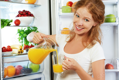 happy woman drinking orange juice about refrigerator