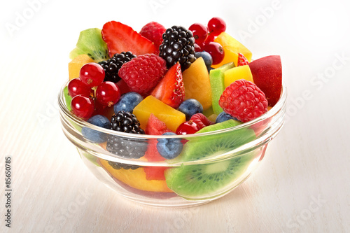 fresh fruit salad in glass bowl isolated on beige wood table