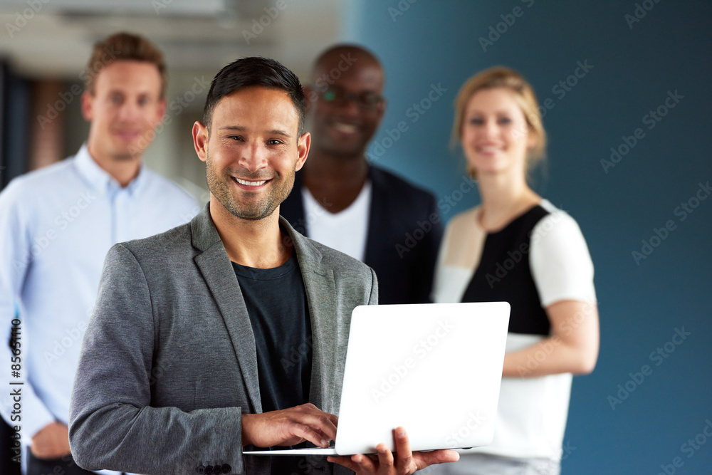 Young white executive holding laptop with colleagues in background