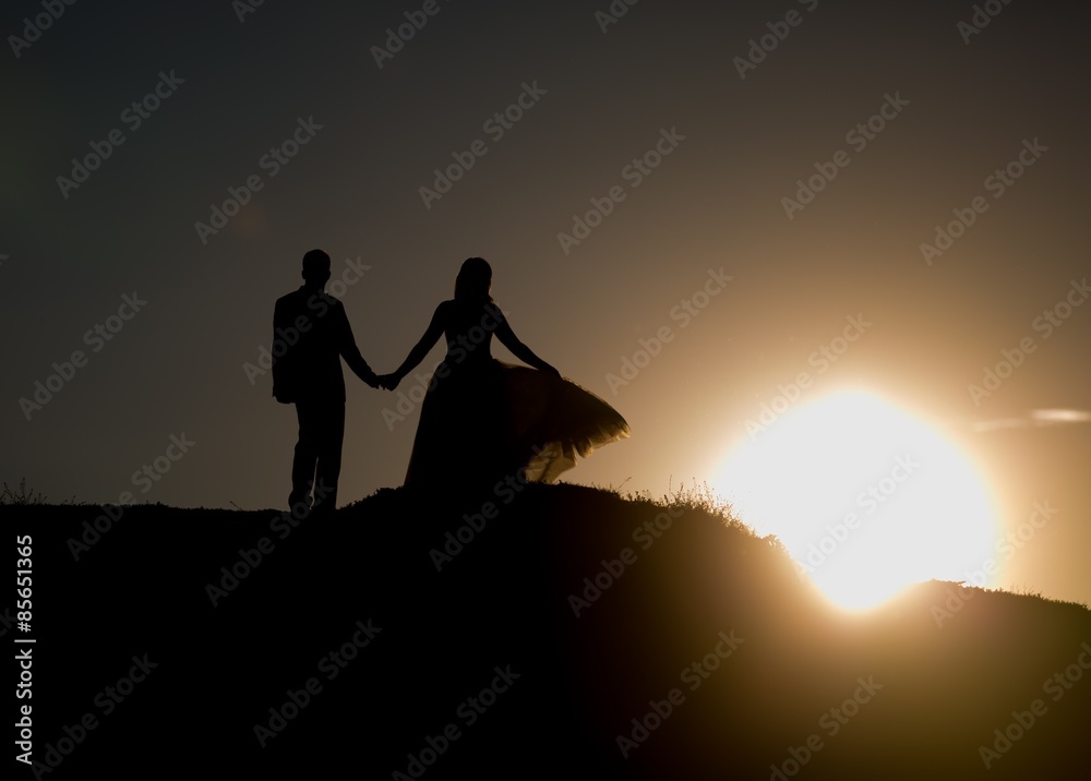 Silhouettes of wedding couple standing on hill.