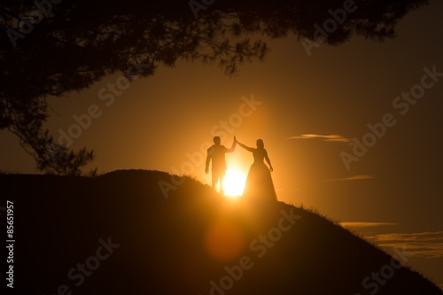 Silhouettes of wedding couple standing on hill.