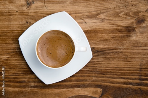 Coffee in white cup on a saucer on a wooden table