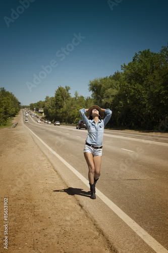 Young beautiful woman hitchhiking along a road