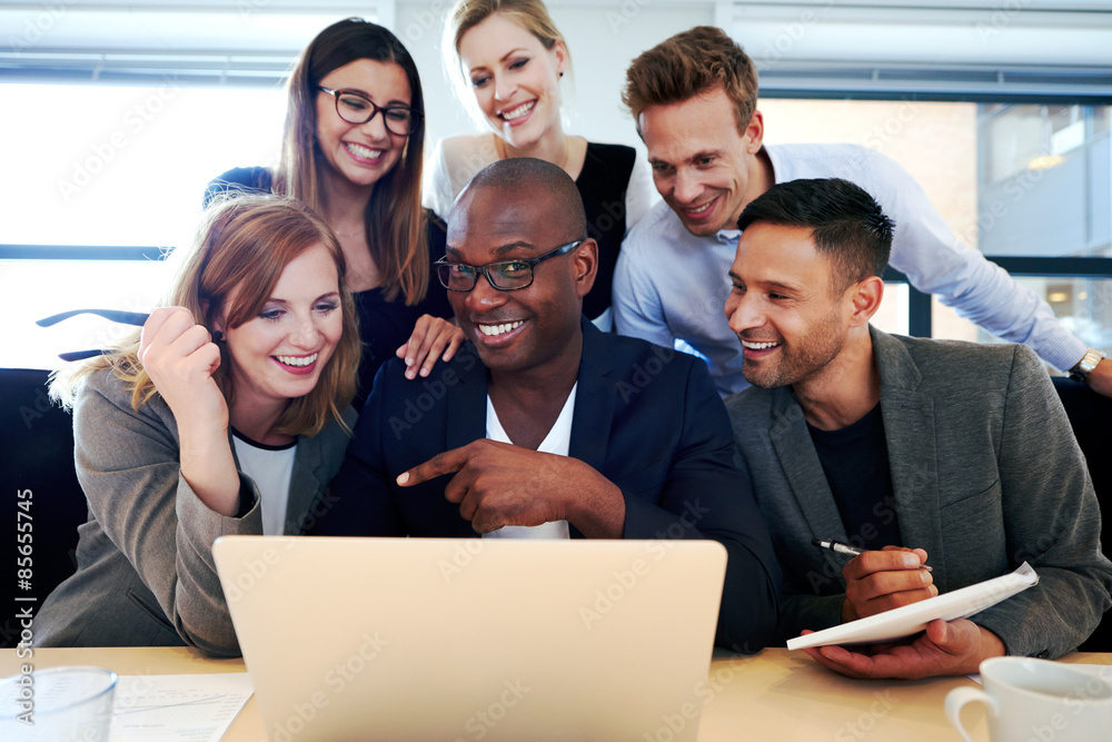 Group of executives smiling gathered around laptop Group of executives smiling gathered around laptop