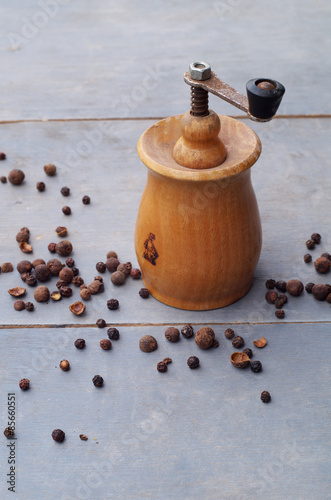 Old rustic pepper mill and peppercorns on wooden backround