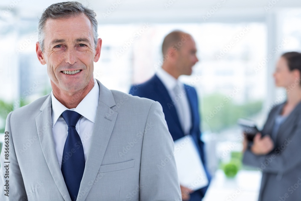 businessman smiling with two colleague behind him businessman smiling with two colleague behind him
