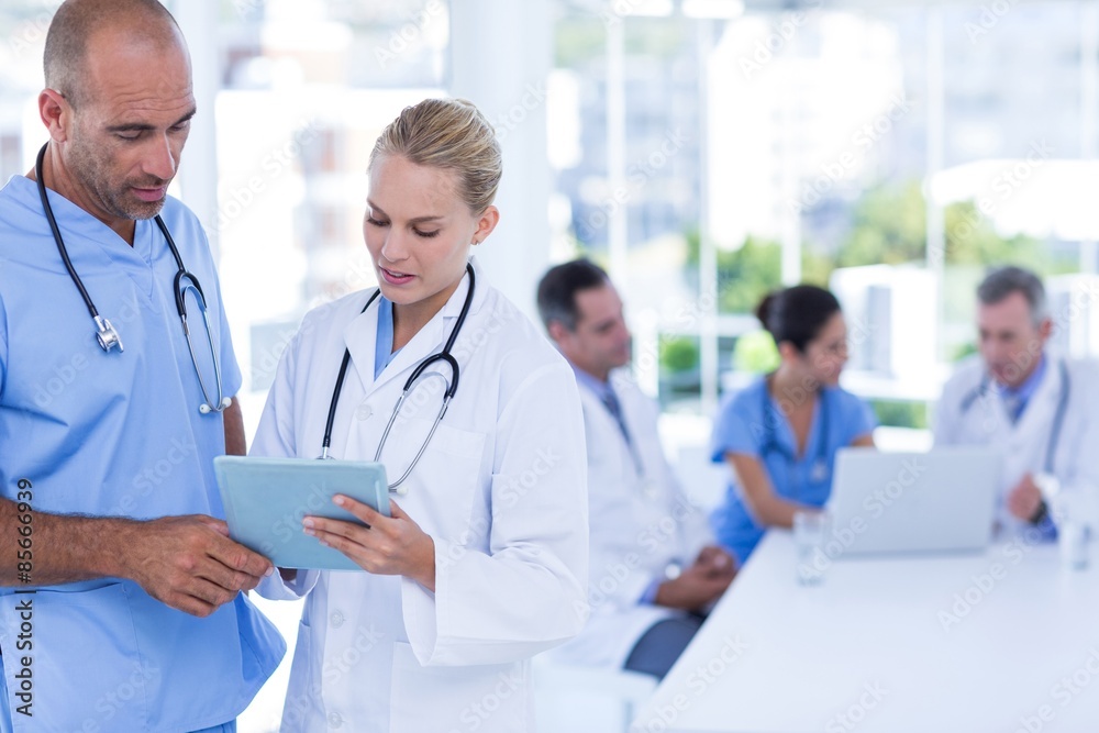 Two doctors holding clipboard while their colleagues working Two doctors holding clipboard while their colleagues working