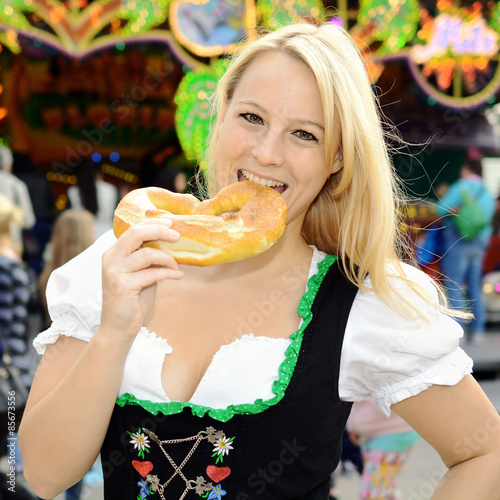 Madl in Dirndl als bayrische Tracht isst Brezel als Laugengeb  ck und Snack zum Oktoberfest