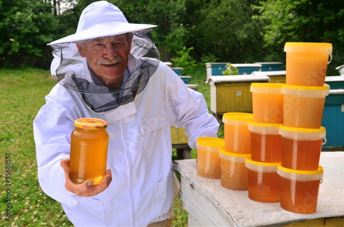 pszczelarz w pasiece prezentujący słoik świeżego miodu