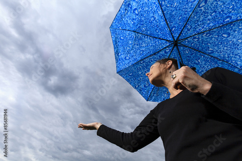 Looking up at woman holding umbrella with dark clouds in the sky.