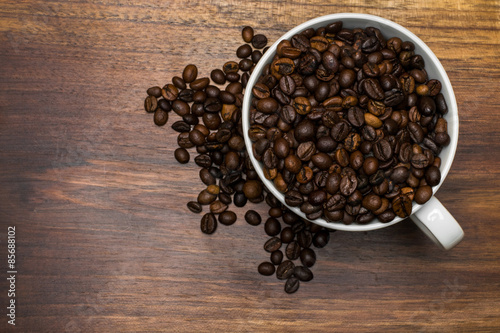 Cup full of coffee beans over wooden background