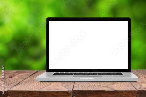 Laptop with blank screen on wooden table on green