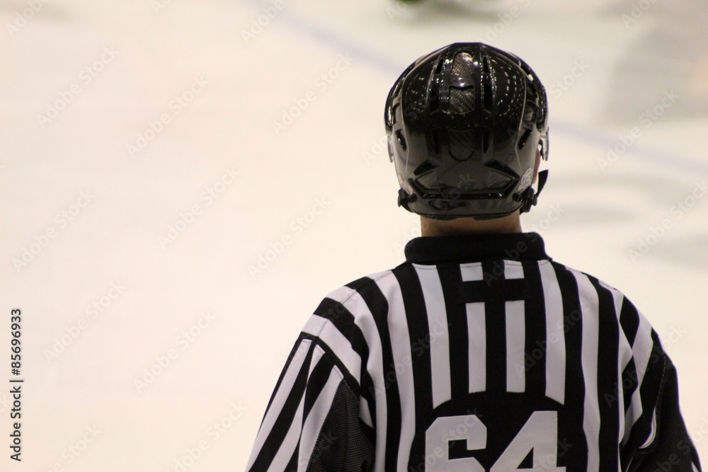 Naklejka premium The back of a hockey referee on the ice during a hockey game. He is wearing a helmet and standard uniform.