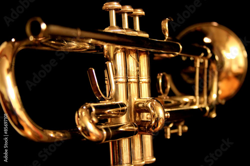 A golden brass trumpet with a black background. The keys are in focus with the bell of the trumpet being blurry.