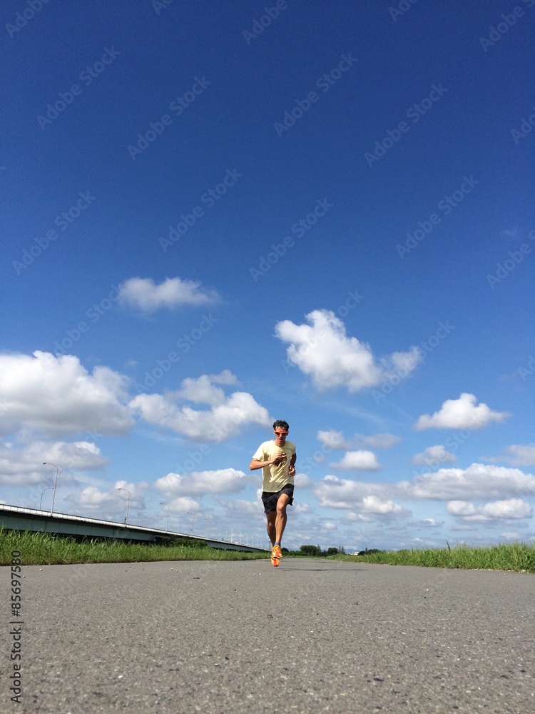 Runner on straight open road with fluffy clouds and blue skies behind Runner on straight open road with fluffy clouds and blue skies behind