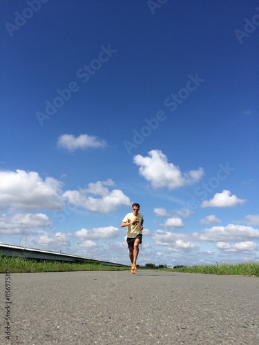 Runner on straight open road with fluffy clouds and blue skies behind