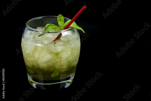 A Mint Julep, the official drink of the Kentucky Derby, with fresh mint leaves, crushed ice, and a red stir stick with a black background. Drink is oriented on the left side of the photo.