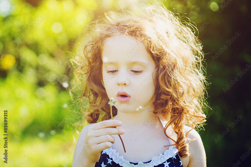 Little curly girl blowing dandelion in sunset. Background toning Little curly girl blowing dandelion in sunset. Background toning