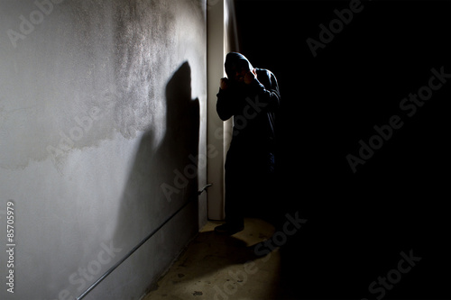 Vászonkép hooded criminal stalking in the shadows of a dark street alley