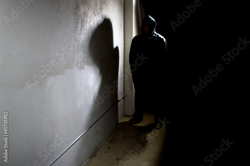 hooded criminal stalking in the shadows of a dark street alley photo