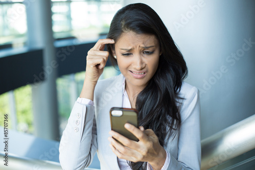 Closeup portrait, smart pretty young female in gray white suit, dumbfounded flabbergasted by what she sees on cell phone, isolated indoors office background