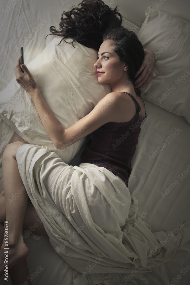 Woman sending a text message while lying in bed Woman sending a text message while lying in bed