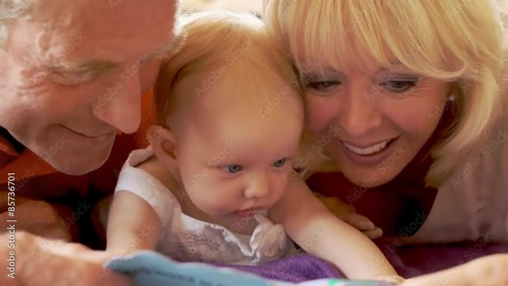 Grandparents and baby granddaughter lying on floor reading book. Grandparents and baby granddaughter lying on floor reading book.