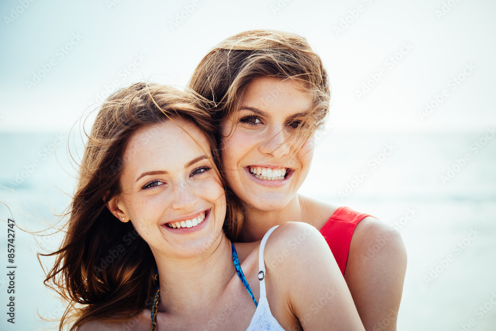 Beach in summer. A couple of young women in swimwear hugging affectionately in the sun on a summer day. Close-up photo of the smiling faces