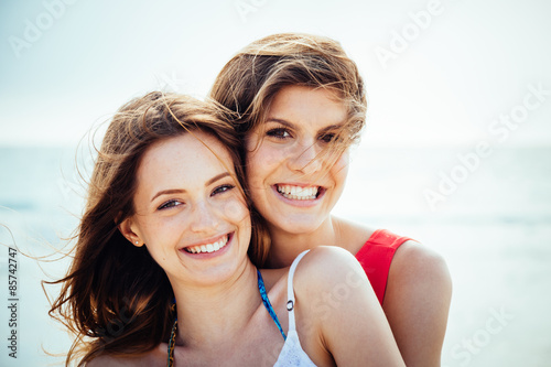 Beach in summer. A couple of young women in swimwear hugging affectionately in the sun on a summer day. Close-up photo of the smiling faces © loreanto