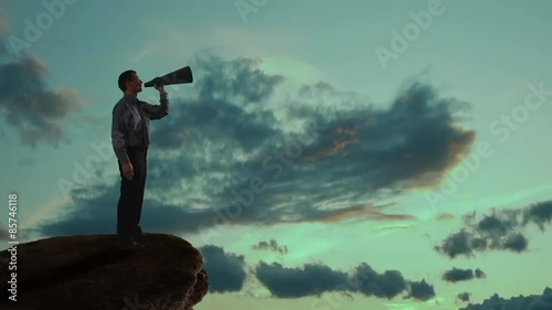 Businessman talking into a megaphone on a mountain. 