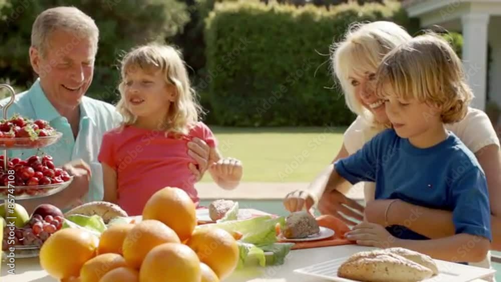 Grandparents and grandchildren playing and sitting at table of food in garden. Grandparents and grandchildren playing and sitting at table of food in garden.