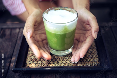 Woman holding Matcha green tea latte on wooden table