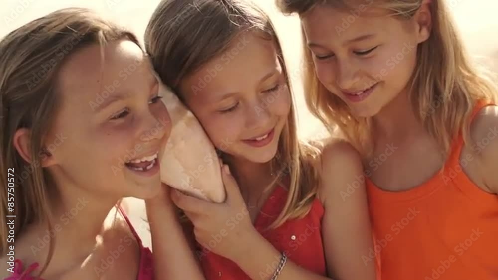 Three girls playing on beach listening to conch shell.