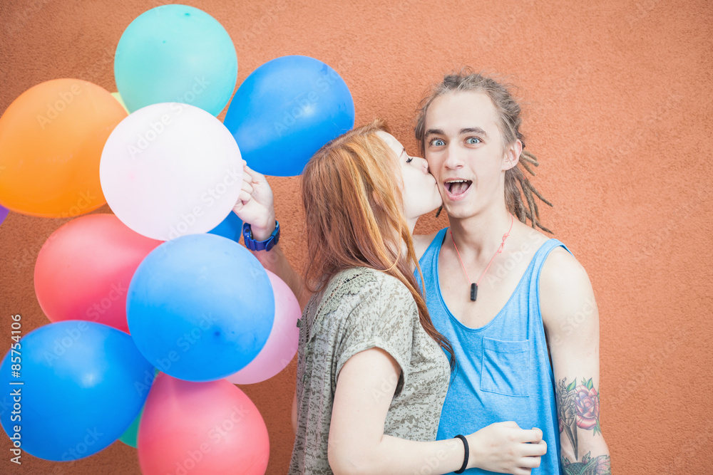Young happy couple near the orange wall stand with balloons Young happy couple near the orange wall stand with balloons
