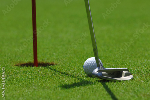 Golf player at the putting green hitting ball into a hole 