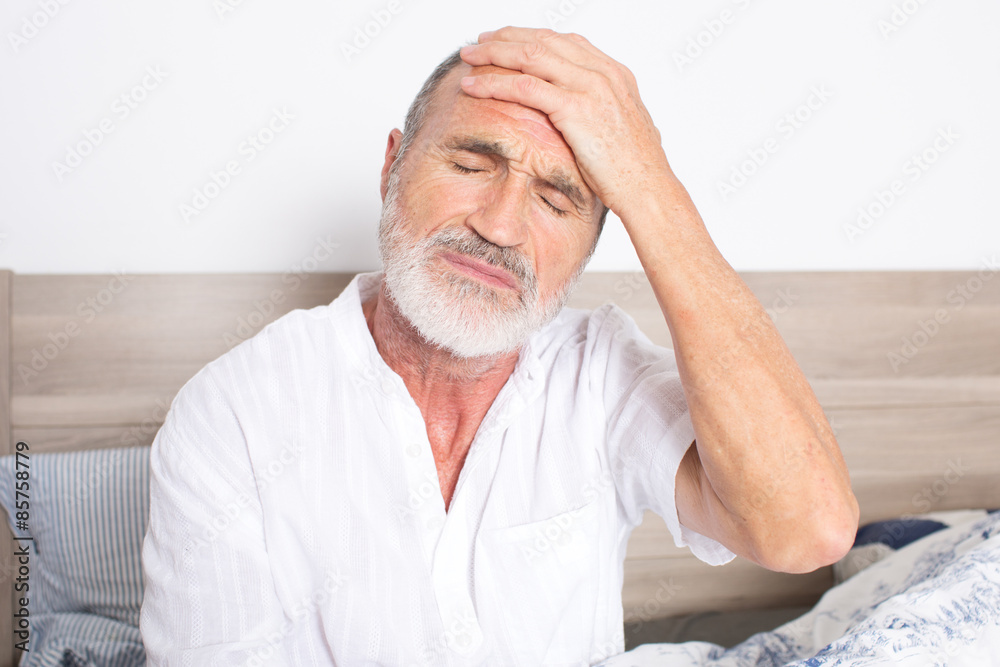 Elderly man sitting on bed suffering from headache Elderly man sitting on bed suffering from headache